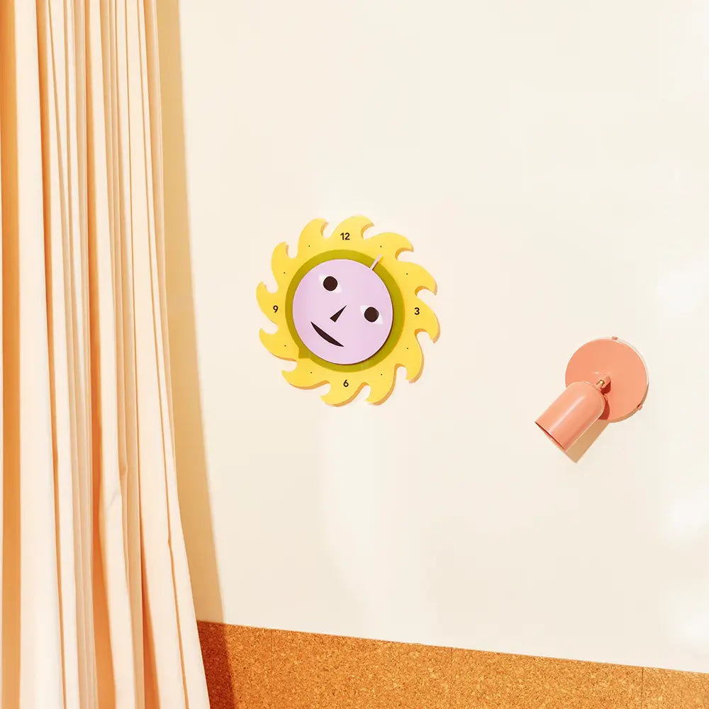 Sun-shaped wall clock with a smiley face on a light beige wall.