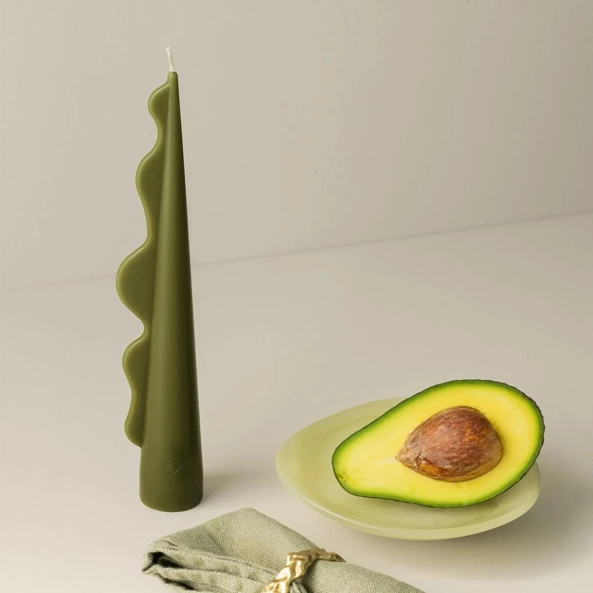 Green wavy pillar candle next to an avocado half and a green napkin.