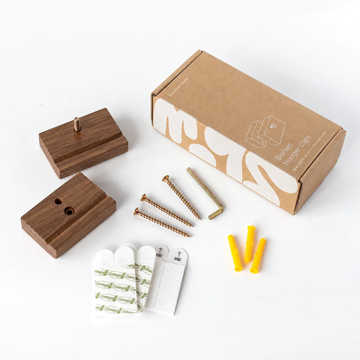 A blanket hanger set of 3 clips in walnut with a kit laid out on a white background, including 3 screws, 3 wall anchors, 3 white adhesive hooks, an Allen key and a brown packaging box.