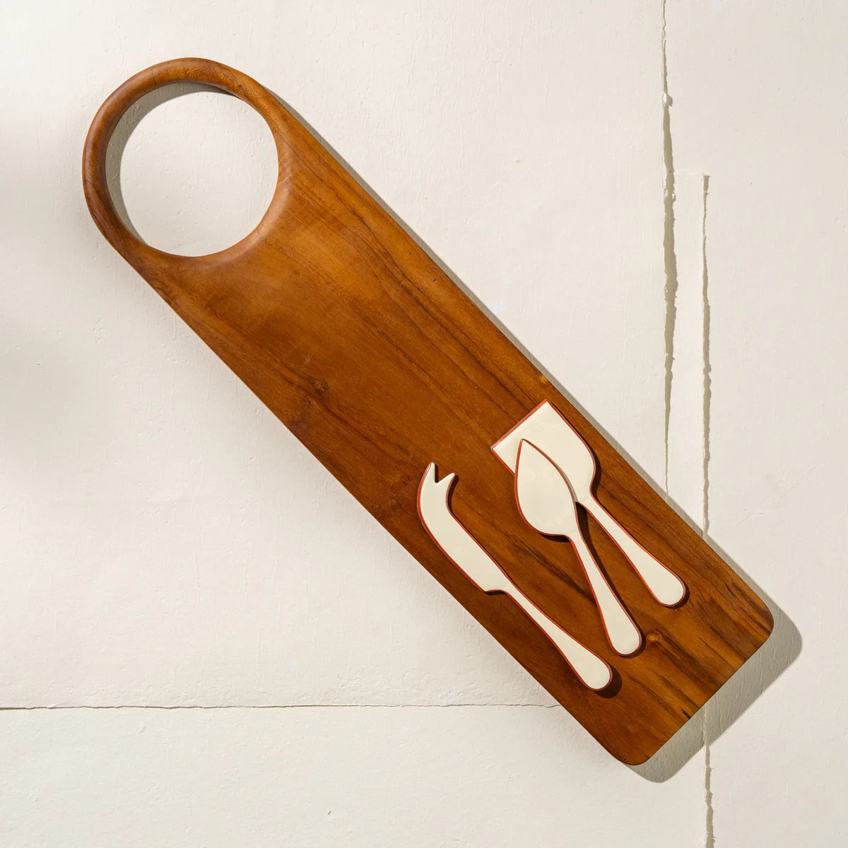 Lifestyle shot of a set of 3 enamel coated stainless steel cheese knives. Cream coloured with a burnt orange outline around the edges.