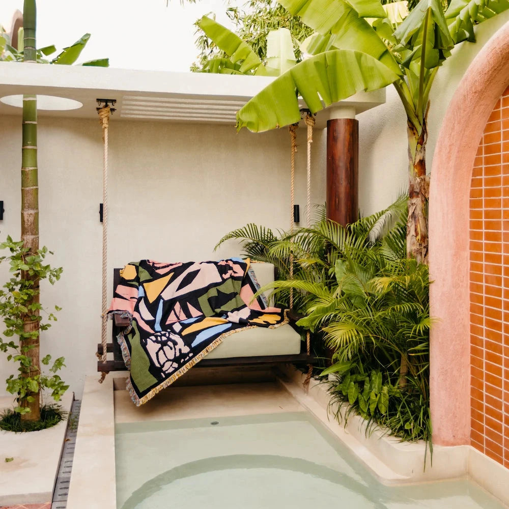 Outdoor relaxation area with a swing, colorful blanket, and lush greenery.