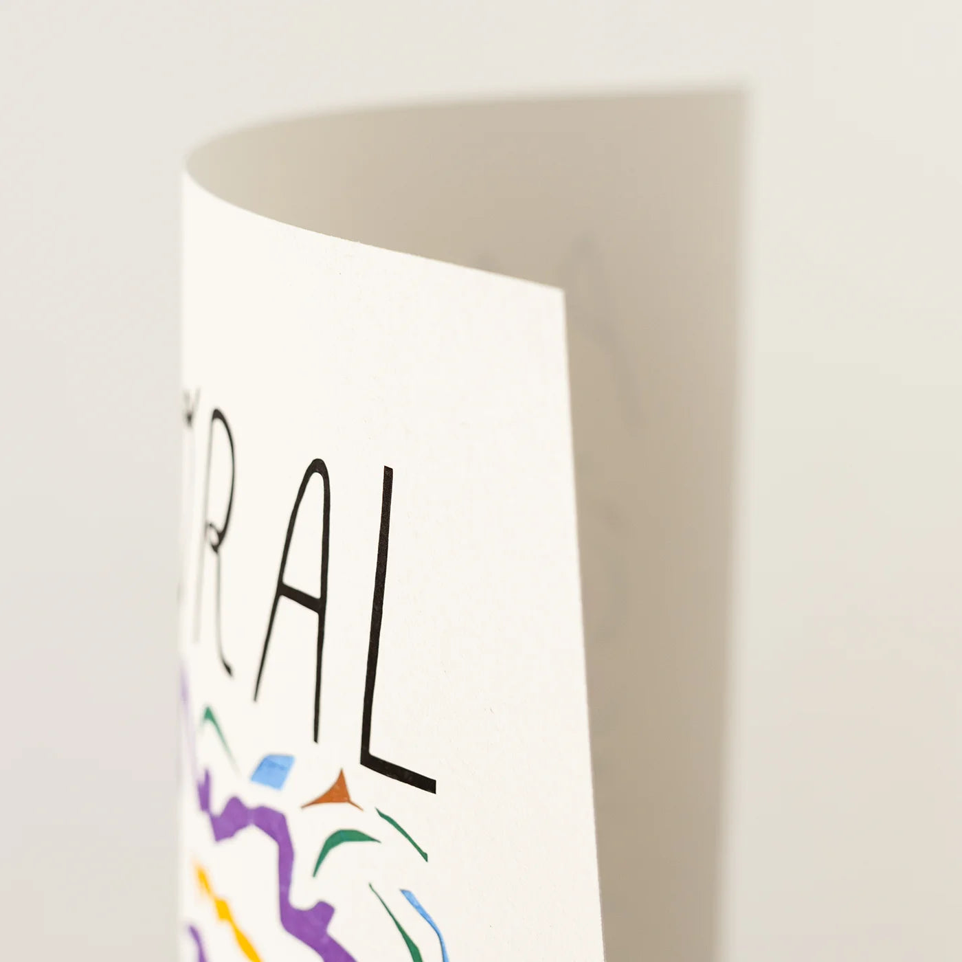 A close-up of a white art print showing partial black text and colorful abstract line art on a light neutral background.