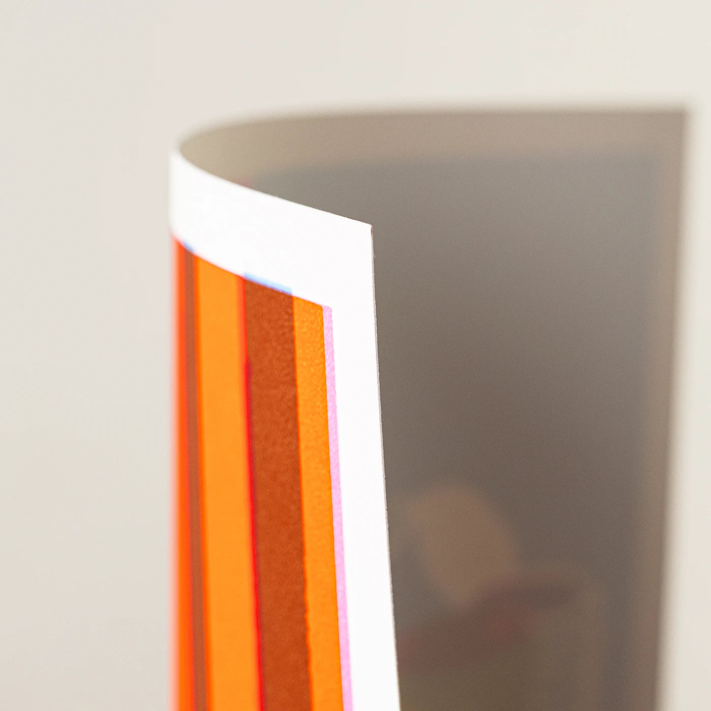 A close-up of an art print with bold vertical orange and peach stripes, showing a white border. Photographed against a light neutral background.