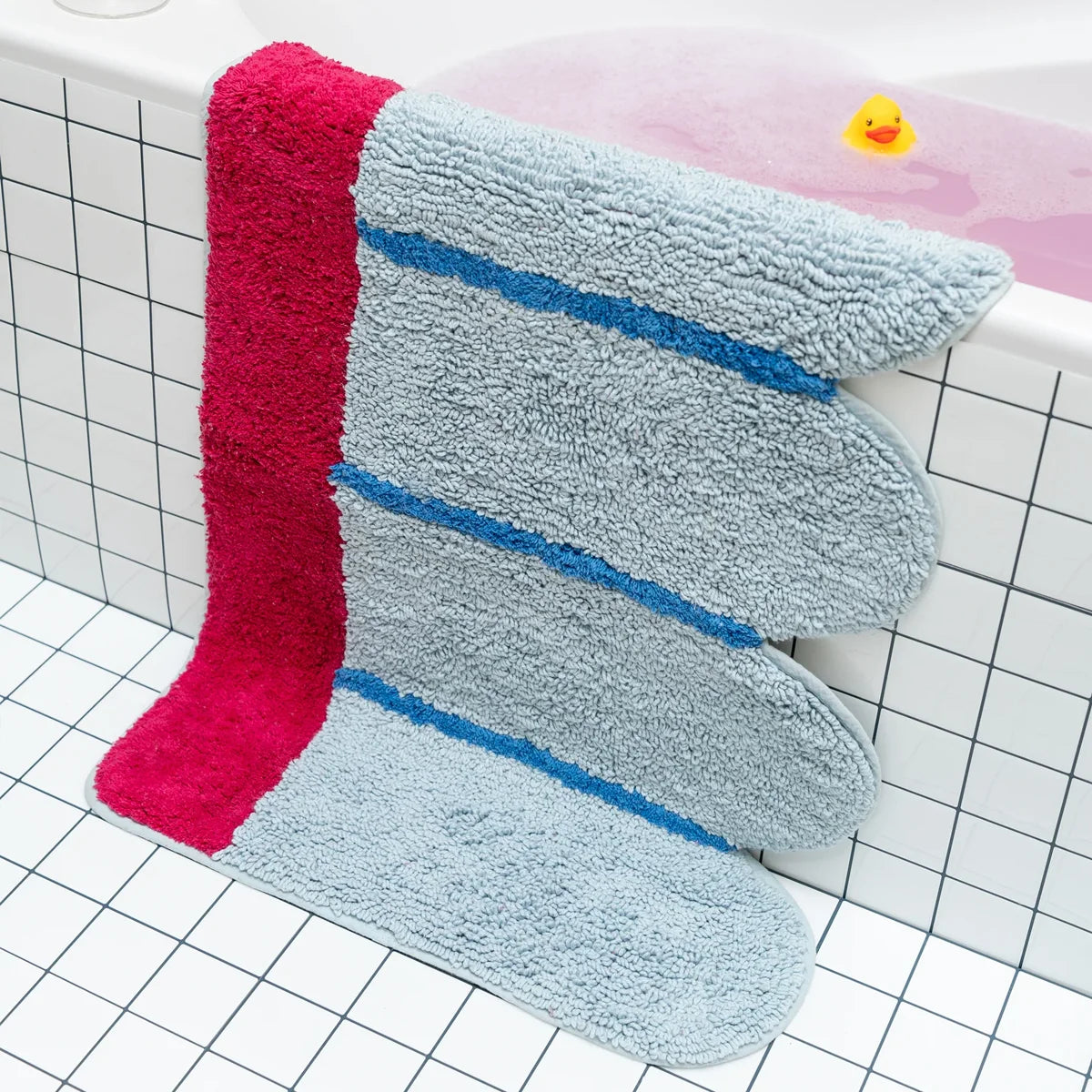 Designer bath mat with blue and pink design on a bathtub with a rubber duck in the background