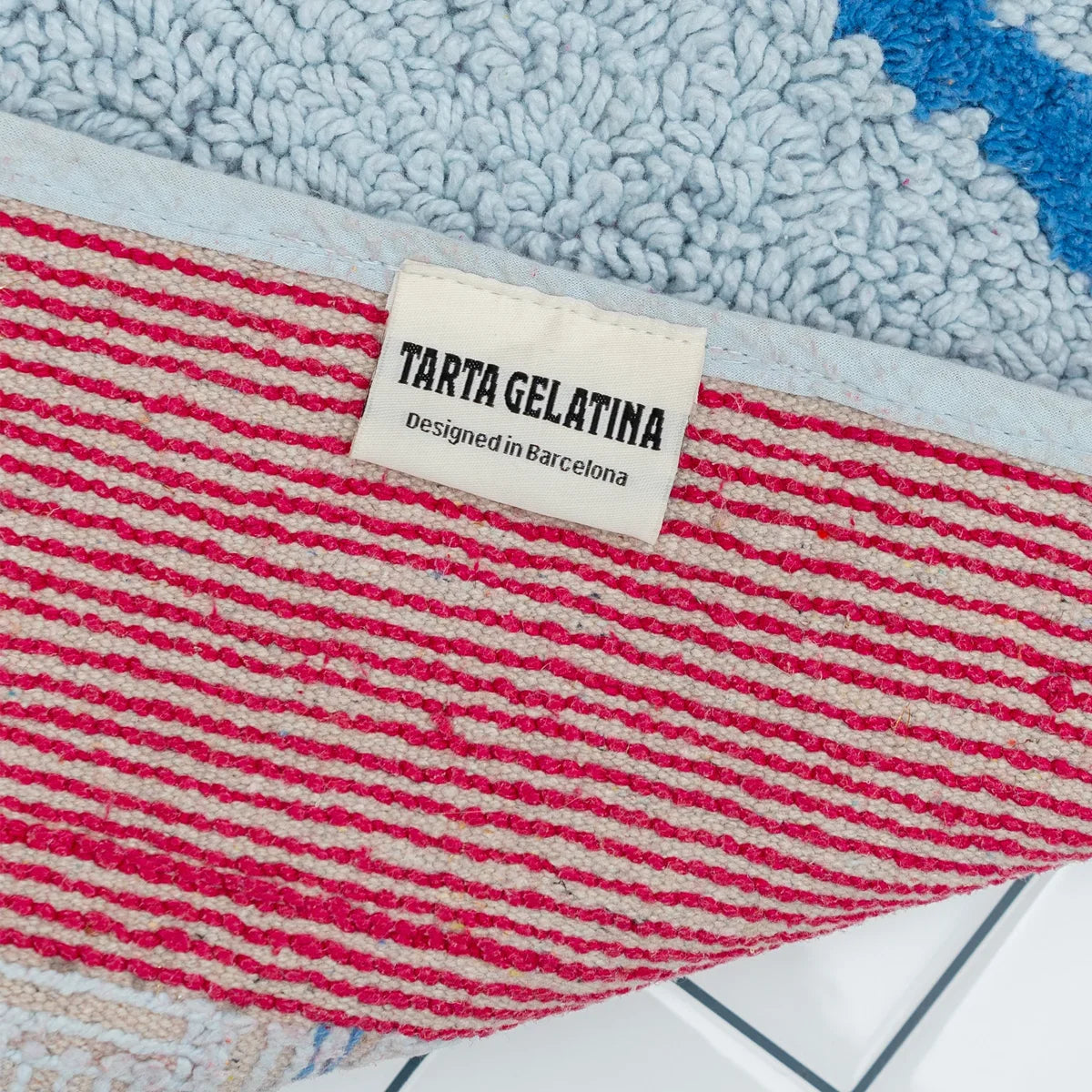 Close up of the Poolside bath mat with blue and pink design, with Tarta Gelatina label