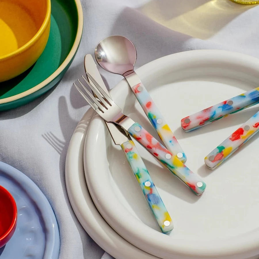 Colorful polka dot cutlery set on a white plate with a yellow bowl and green plate in the background.