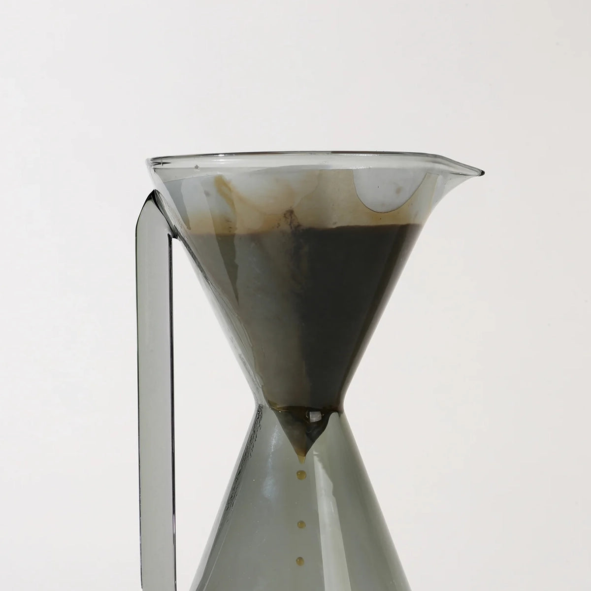 Clear glass coffee dripper with coffee grounds on a white background