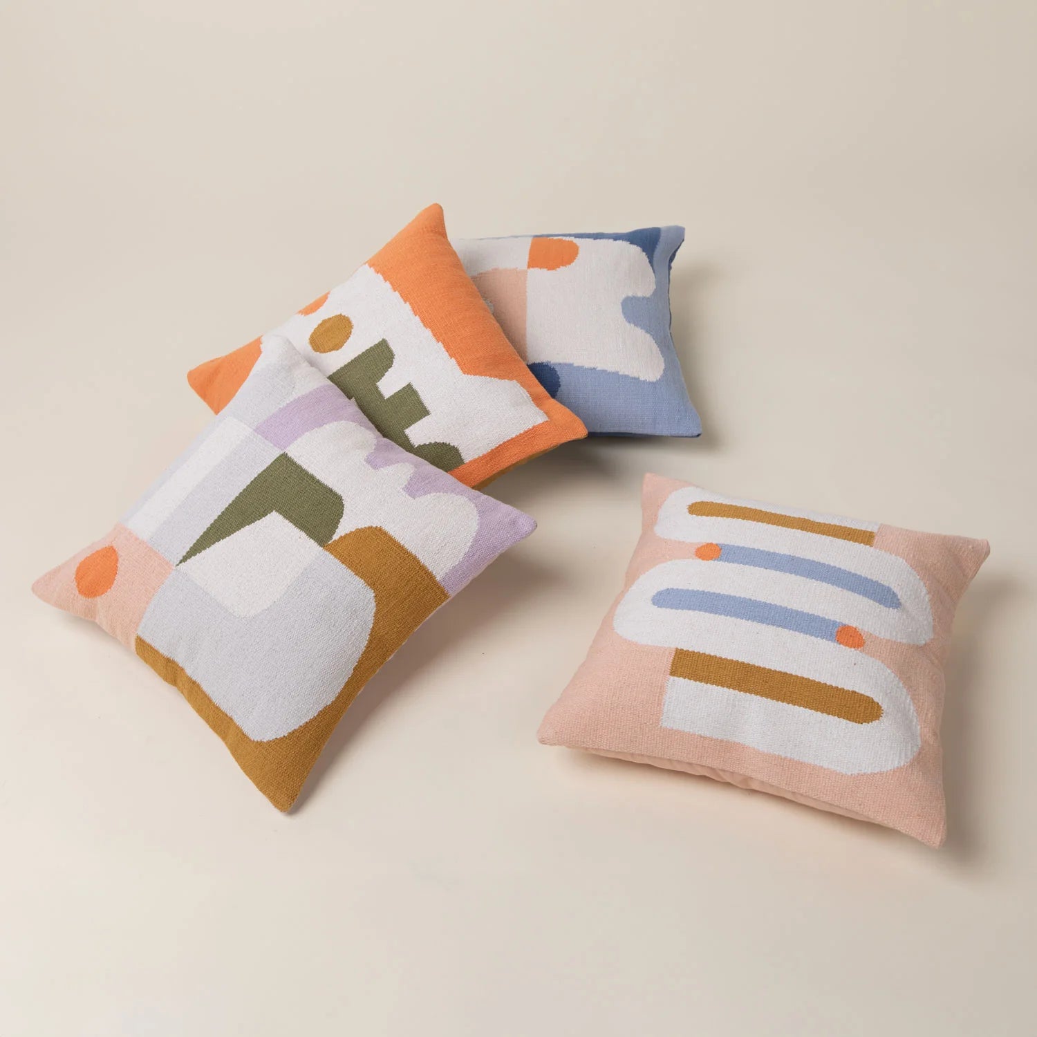 Set of four colorful pillows with abstract designs on a beige background