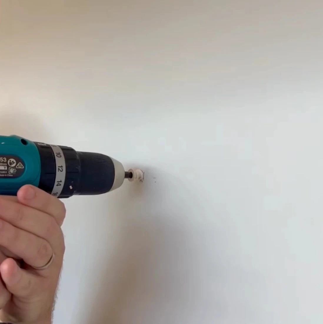 Hand using a drill on a white wall to hang wall tapestry