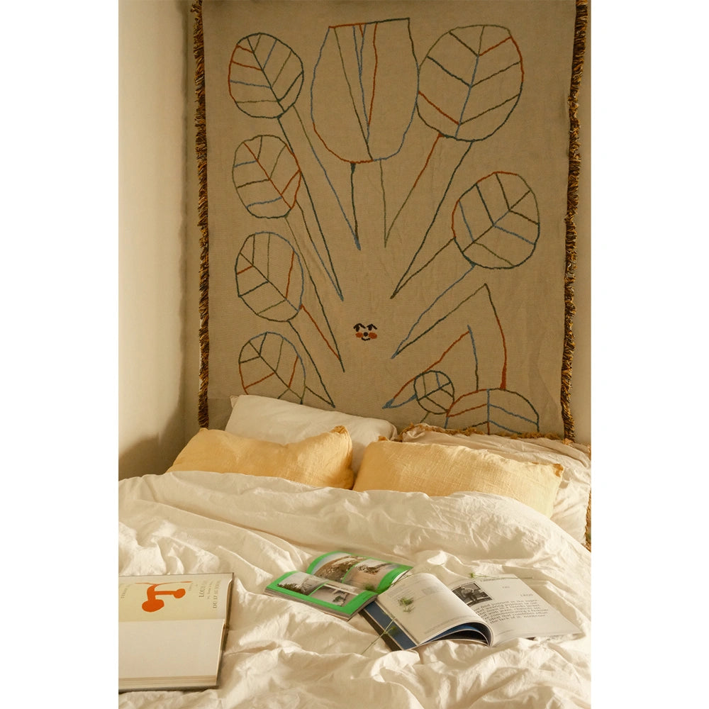 Decorative wall hanging tapestry with leaf pattern above a bed with books and magazines.