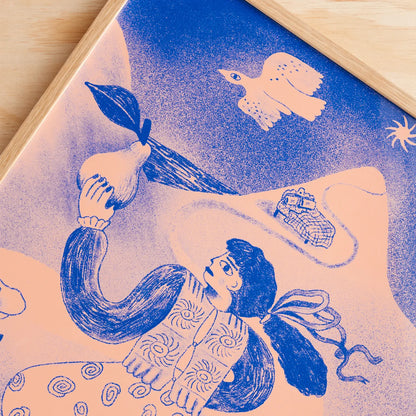 An art print with a wooden frame, featuring a blue and peach illustration of a woman holding a pear, a flying bird, and a small house, shown on a light wood surface.