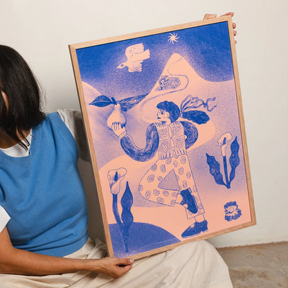 A person seated indoors holds a large framed art print. The artwork features a stylized figure in blue against a soft pink-to-blue gradient background with abstract floral and bird motifs.