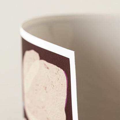 A close-up of an art print, showing a dark burgundy background with a large pale pink abstract shape and a white border, photographed against a soft light gray background.