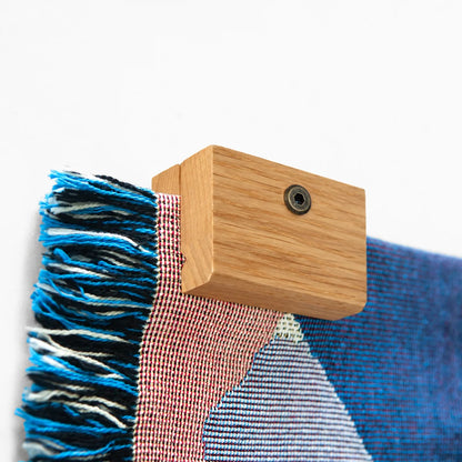 Close up image of a corner of a Slowdown woven blanket being held up on a wall with an Oak blanket hanger clip.