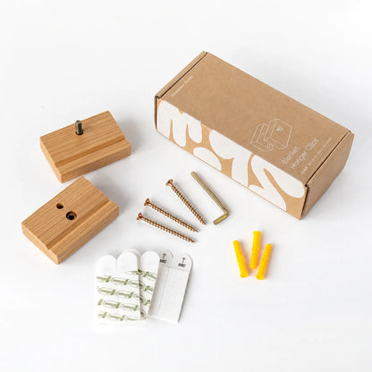 A blanket hanger set of 3 clips in oak with a  kit laid out on a white background, including 3 screws, 3 wall anchors, 3 white adhesive hooks, an Allen key and a brown packaging box.