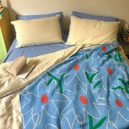 Bed with pale yellow sheets and floral blanket and pillows, framed artwork on the wall