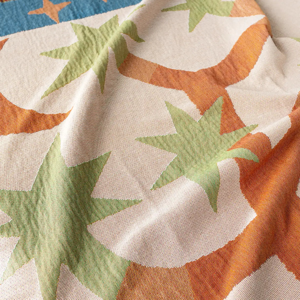 Close-up of woven throw blanket fabric with green and orange star patterns on a beige background