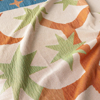 Close-up of woven throw blanket fabric with green and orange star patterns on a beige background