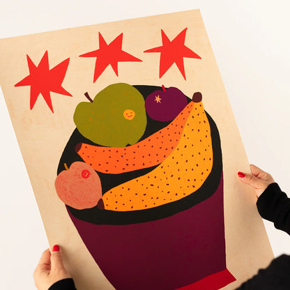 A person holds a large art print featuring a stylized fruit bowl with red stars above, shown against a plain white background.