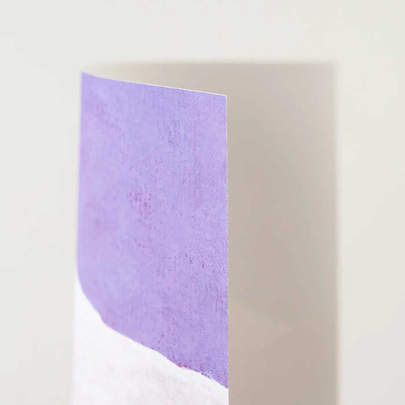A close-up of a vertical rectangular art print with a textured lavender-purple upper section and a white lower section, photographed against a plain light beige background.