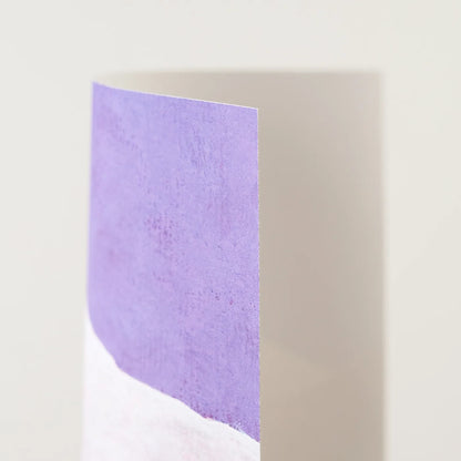 A close-up of a vertical rectangular art print with a textured lavender-purple upper section and a white lower section, photographed against a plain light beige background.