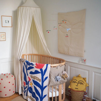 Nursery room with a crib, decorative blanket, and wall art. A baby blanket with flower and butterfly design hangs over the cot. 