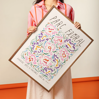 A person holds a large framed art print featuring a colorful floral design with the text &