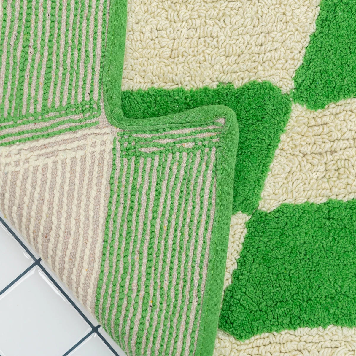 Close up of texture of green and beige textured rug on a tiled floor