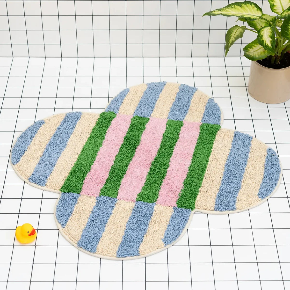 Colorful striped bath mat on a grid background with a rubber duck and plant.