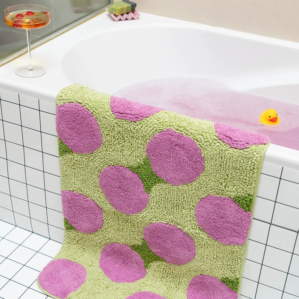 Green bath mat with pink polka dots on a bathtub.