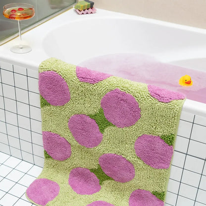 Green bath mat with pink polka dots on a bathtub.