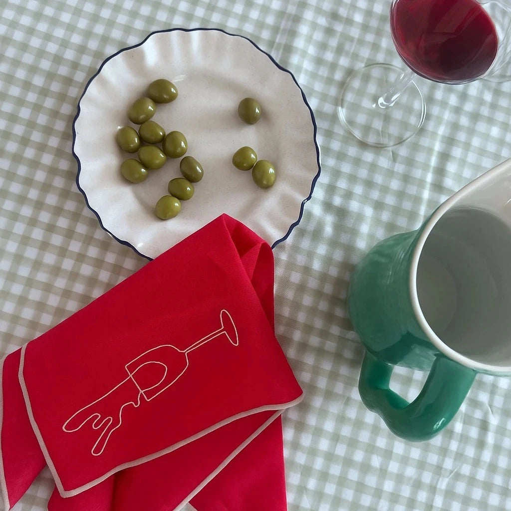Green peas on a white plate with a red napkin and green mug on a checkered tablecloth.