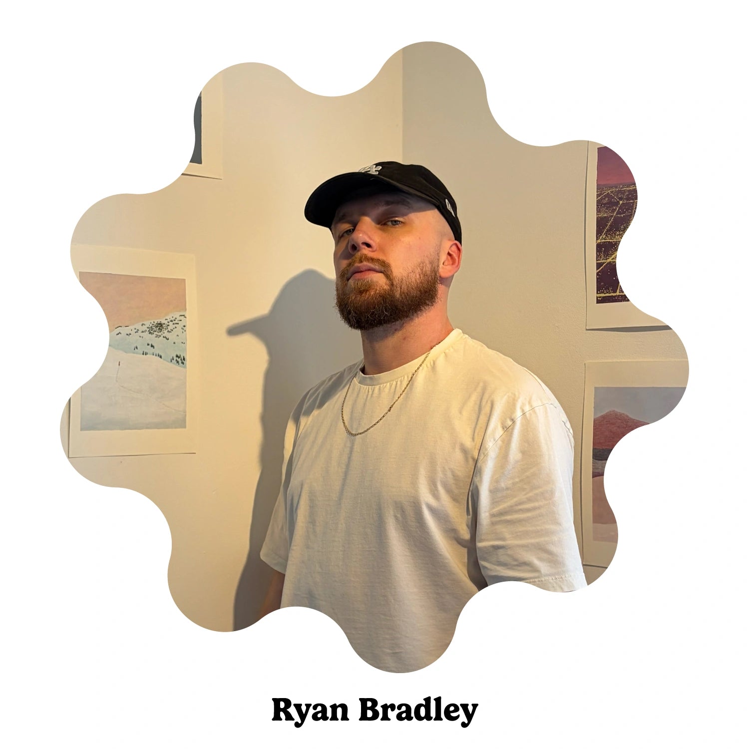 Portrait of English artist Ryan Bradley wearing a black baseball cap and a white t-shirt, standing in an indoor setting with framed art on the wall. The image is presented in a decorative scalloped circular frame with the text &