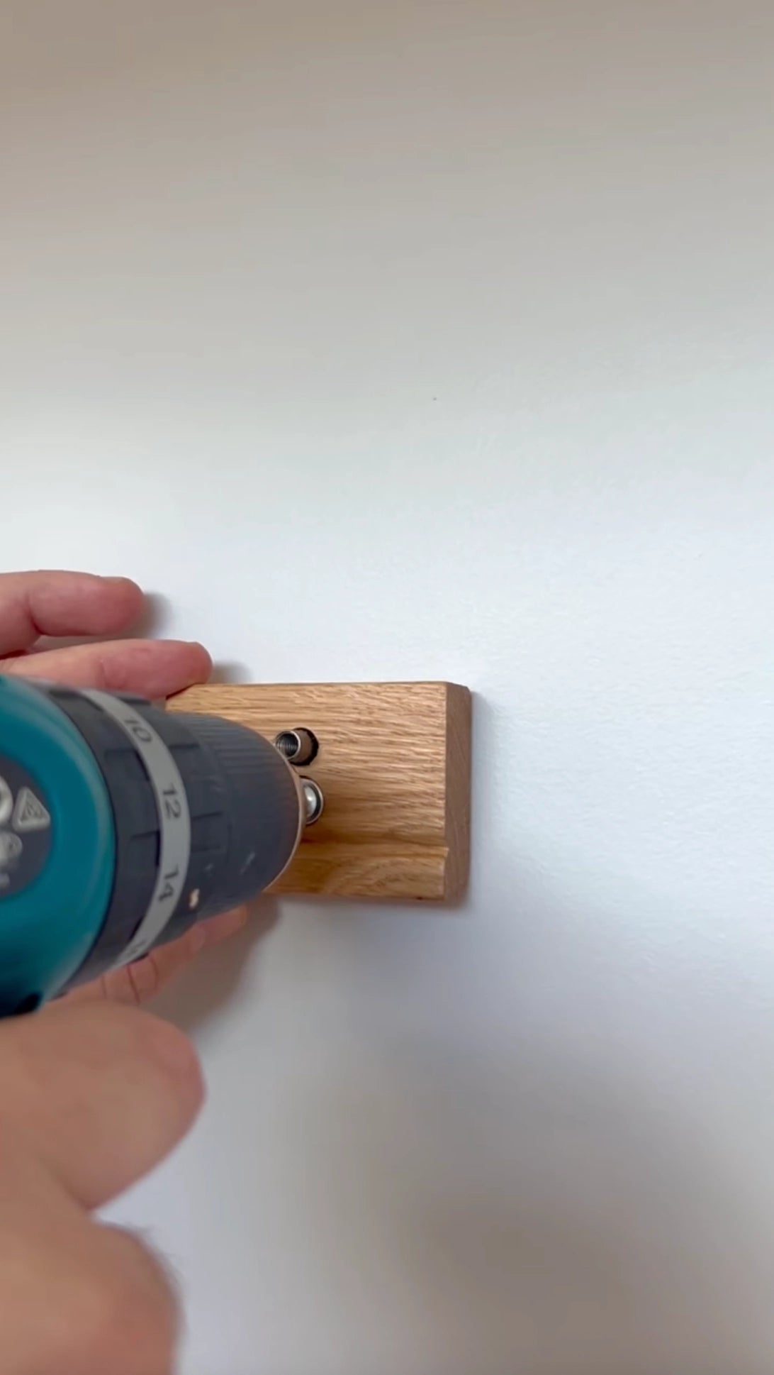 Person using a drill to attach a tapestry hanger clip to a wall. Used to attach a tapestry blanket